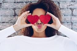 Valentine Day Love Beautiful concept . Happy African American girl holding two hearts on her eyes. 