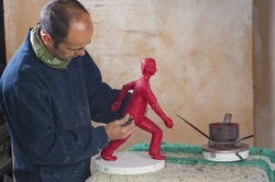 Artisan casting wax on a red statue