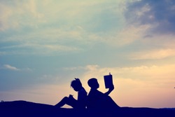 Silhouette of happy boy and girl reading a book in the sky sunset ,free time on holiday