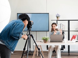 Asian camera man and pretty influencer recording live video about game product review with microphone and share screen from laptop device for broadcast on channel or social media in home studio setup