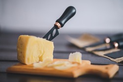 Composed cloesup detail view of aged cheddar cheese with cheese knife set, over vintage brown wooden backdrop
