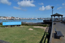 Photography of a wooden pier and a gazebo and the boats anchored at  the port of Punta del Este City, Uruguay and a sign saying Port of Punta del Este in spanish