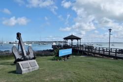 Photography of a wooden pier and a gazebo and the boats anchored at  the port of Punta del Este City, Uruguay and a sign saying Port of Punta del Este in spanish and an anchor