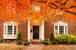 Red brick house entrance with seasonal wreath on door and porch and bay windows on autumn day with leaves on the ground and hydrageas still in bloom - colorful foliage