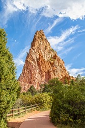 Walking path with rustic fence through trees and past jutting red stone outcropping at Garden of the Gods in Colorado Springs Colorado USA