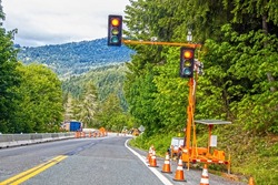 Portable solar powered traffic light at construction site in tree covered mountains with equipment and traffic cones