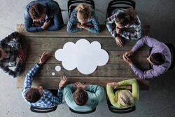 Hipster business teamwork brainstorming planning meeting concept, man tells his opinion, people sitting around the table with white paper shaped like dialog cloud