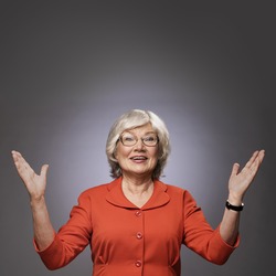 Happy senior lady with hands up on gray background with copy space. Finally! Thanks god! Thanks lord! Excitement concept.