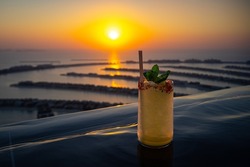 Yellow cocktail on the edge of an infinity pool with a beautiful panorama of the Palm Jumeirah Dubai during sunset