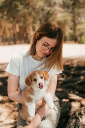 On a picnic in the forest on the shore of a lake, river, sea. A young housewife holds her pet dog in her arms. A cute puppy of the Welsh corgi Pembroke breed and a girl are smiling cheerfully.