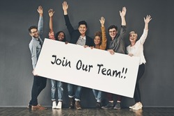 Come and join our team. Studio shot of a diverse group of people holding up a placard against a grey background.