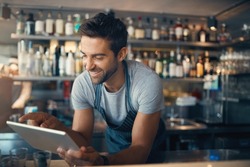 Streamlining small business tasks with smart tech. Shot of a young man using a digital tablet while working behind a bar counter.