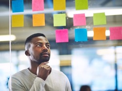 Working his way to success with a well constructed plan. Shot of a young man having a brainstorming session with sticky notes at work.