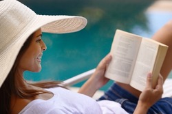 The perfect holiday read. Shot of a young woman reading a book by the poolside.