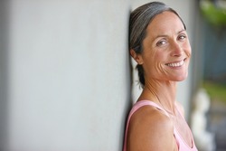 Happiness is an inside job. Portrait of an attractive mature woman in gymwear leaning against a gray wall.