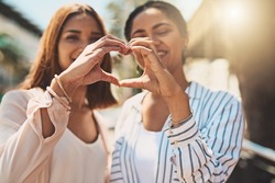 Love keeps your friendships strong. Shot of two cheerful young women forming a heart shape with their hands together while standing outside during the day.