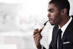 Vaping in style. A young businessman smoking an electronic pipe in an office.