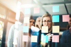Marketing ideas that match the company brand. Shot of a group of businesspeople arranging sticky notes on a glass wall in a modern office.