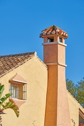 Chimney designed on roof of orange painted house building outside against blue sky background. Construction of exterior architecture of escape chute built on rooftop for fireplace smoke and heat