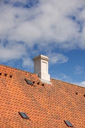 Chimney designed on slate roof of house building outside against blue sky with white clouds background. Construction of exterior escape chute built on rooftop for fireplace smoke and heat from below