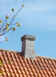 Grey brick chimney designed on slate roof of house building outside against blue sky background. Construction of exterior architecture of escape chute built on rooftop for fireplace smoke and heat
