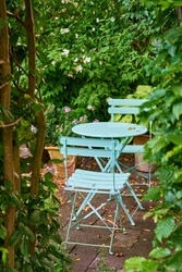 Two green metal chairs and table in a serene, peaceful private courtyard in a home backyard on a summer day. Small outdoor patio furniture set, seating in empty and tranquil garden with fresh plants