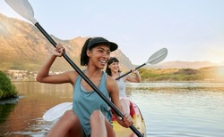 Two smiling friends kayaking on a lake together during summer break. Smiling and happy playful women bonding outside in nature with water activity. Having fun on a kayak during weekend recreation