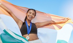 Portrait of a young fit indian female athlete cheering and holding India flag after competing in sports. Smiling fit active sporty woman feeling motivated and celebrating