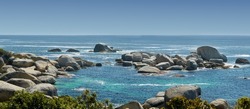 Landscape of large rocks in the ocean in summer. Many stones by the wide, empty seaside. Smooth rocks or cliffs by the beach with light foamy waves at the surface, Hout Bay, Cape Town, South Africa