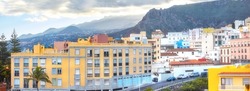 Scenic landscape view of vibrant houses, traditional residential buildings or city structures. Tourism destination street on Santa Cruz road, La Palma, Spain with background mountains and cloudy sky