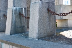 Closeup of concrete structures on the promenade by a harbour with copy space. Rusty chains hanging between stone pillars on a pier outside. A large barrier surrounding a bricked dock surface outdoors