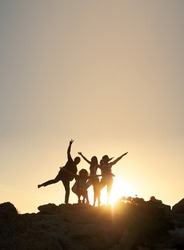 Group of friends posing standing on rocks at sunset having fun summer vacation lifestyle celebrating friendship