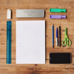 School supplies, stationary or equipment for young working and studying students top view. Assortment, variety or array of education essentials items including a phone and notebook on a wooden desk