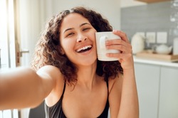 Happy, morning coffee and selfie while smiling and holding cup against her face for warmth while sitting at home. Portrait of a cheerful young woman enjoying her free time and a hot beverage