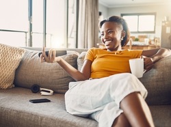 Relaxed, carefree and smiling young female watching tv and streaming movie at home on her living room sofa. Happy, casual and comfortable woman sitting on her couch and enjoying her leisure free