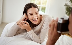 Beautiful, attractive and happy woman having a home photoshoot while lying in bed and smiling. Young excited female having pictures or photos taken while relaxing in her bedroom
