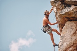 Man mountain or rock climbing while cliff hanging and adrenaline athlete on adventure and check safety equipment, hook and rope. Fearless man doing fitness, exercise and workout during extreme sport