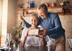 Love, couple elderly and gift to celebrate anniversary on date with smile, happy and excited together. Romance, mature man and older woman exchange present relax, being loving and bonding at home.