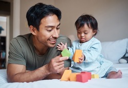 Baby, down syndrome and learning on a bed with child and father playing with educational blocks in a bedroom. Family, disability and kids bonding with asian parent, relax with creative activity