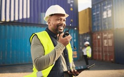 Logistics, radio and a black man in shipping container yard with tablet. Industrial cargo area, happy transport worker talking on walkie talkie in safety gear and working for global freight industry.