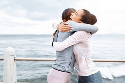 Fitness, friends and women hug at the ocean, success and workout goals, celebration of teamwork with personal trainer. Health, exercise and training target, happy woman hugging friend at sea waves.