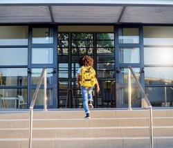 Child, walking and school entrance for education, learning or childhood development at academy building. Kid having a walk up the steps ready for back to school morning with backpack for knowledge