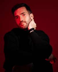 Fashion, man and neon light for aesthetic model in studio for beauty, success and art portrait on red background. Handsome male in black clothes for professional business style magazine cover
