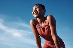 Fitness, black woman and happy athlete smile after running, exercise and marathon training workout. Blue sky, summer sports and run of a African runner breathing with happiness from sport outdoor