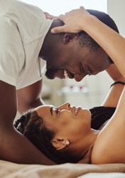 Black couple, love and home bedroom romance while happy and intimate together on bed at home, apartment or hotel. Face of young man and woman in happy marriage with commitment and care on honeymoon