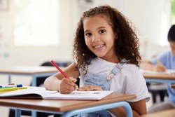 Learning, drawing and portrait of girl in classroom exam, education or studying with book. Preschool smile, development and happy kid or student coloring for creative art in notebook in kindergarten.