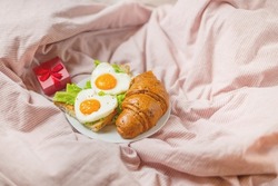 Romantic breakfast in bed. Heart-shaped scrambled eggs on hundreds and a fresh croissant. End of breakfast for Valentine's Day.
