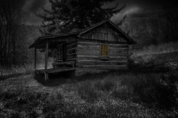 Dark, gritty image of old abandoned house in the woods with a warm glow from inside
