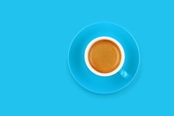 One full morning espresso coffee in small blue cup with saucer on blue paper background, elevated top view, directly above