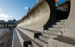 Curved concrete sea wall with concrete steps in foreground. Civil engineering and flood prevention through reinforced coastal sea defenses.